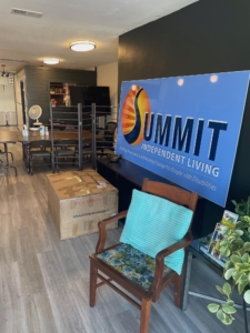 Photograph of Summit's Polson office. On the right is a large sign that reads Summit Independent Living. In front of it are a chair and a table with a house plant.